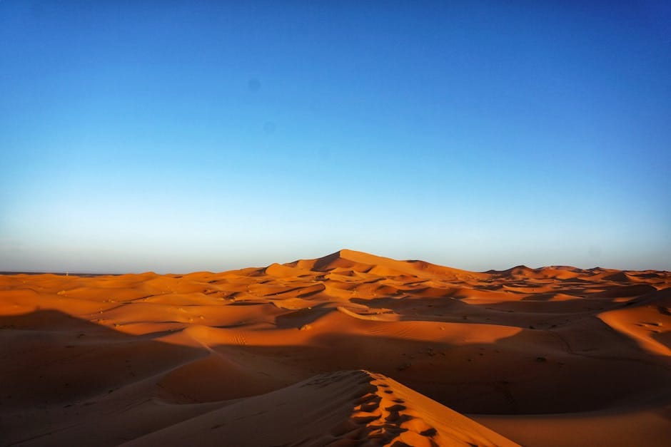 Capture the stunning beauty of expansive orange dunes beneath a vast blue sky, perfect for adventure or travel themes.